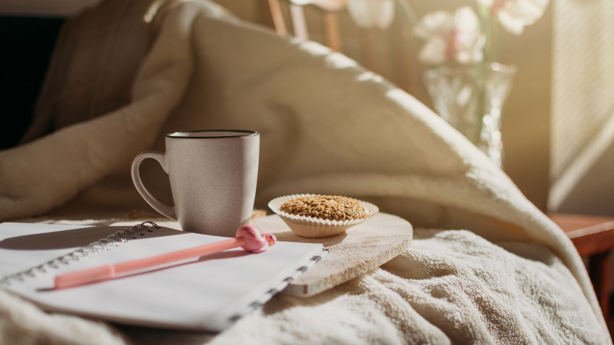 A photo of a notebook, pen, snacks, and mug, on a bed